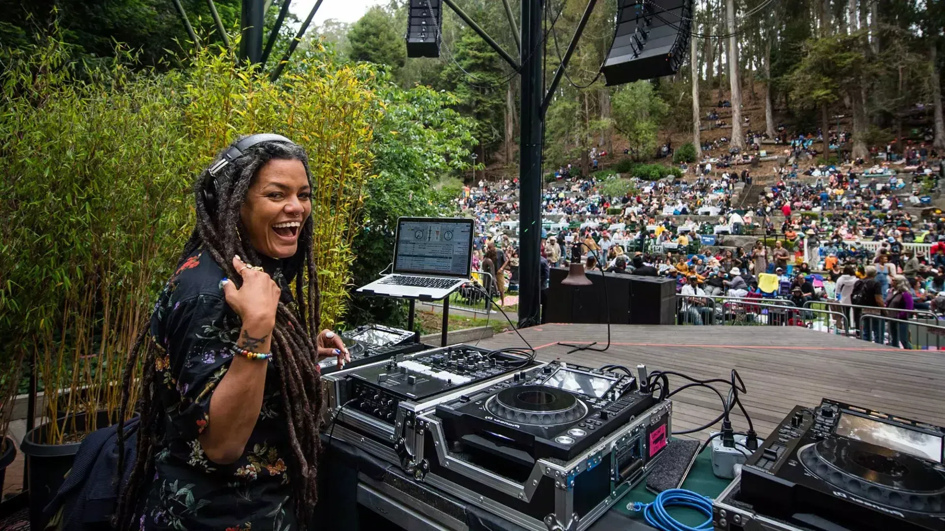 Eine Frau, die beim Stern Grove Festival auflegt, blickt ihr über die Schulter und lächelt in die Kamera.