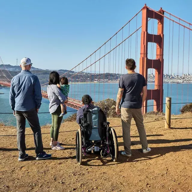 Um grupo de pessoas, incluindo uma pessoa em cadeira de rodas, é visto por trás enquanto olham para a Ponte Golden Gate 吗, Headlands.